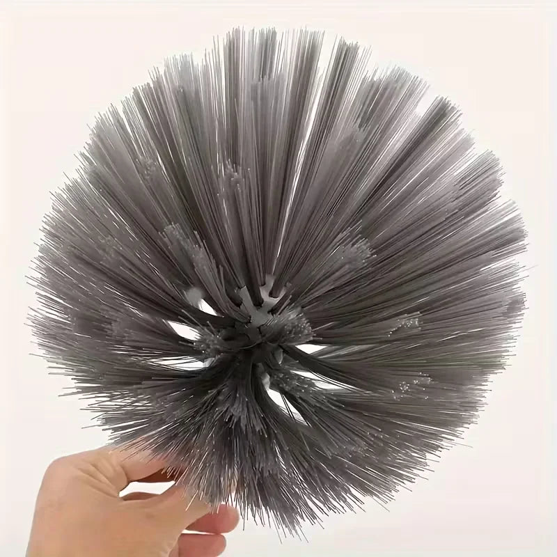 A hand holds a grey metal cleaning broom with stiff bristles, viewed from above.