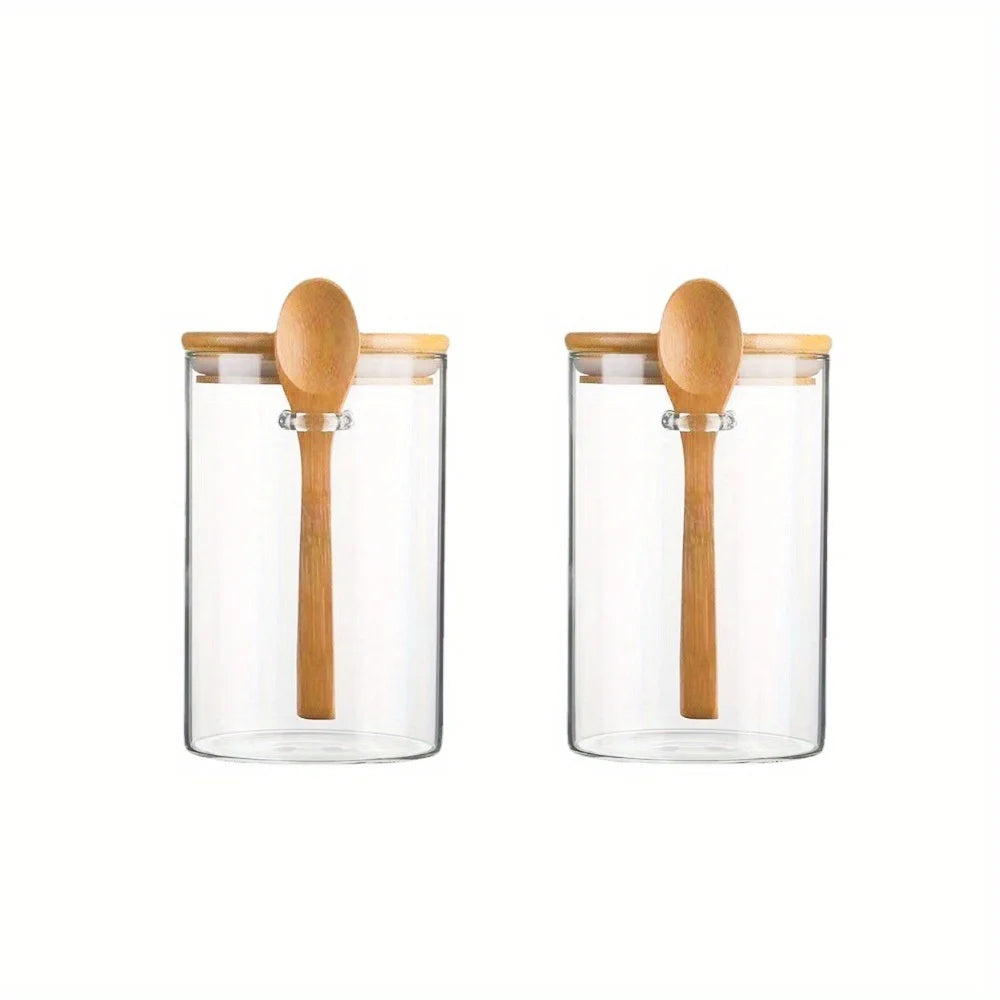 Two clear glass spice jars with bamboo lids standing side by side.