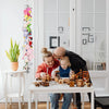 A family is playing with wooden toys on a table in front of a white cabinet with a bohemian cotton hanging storage chain.