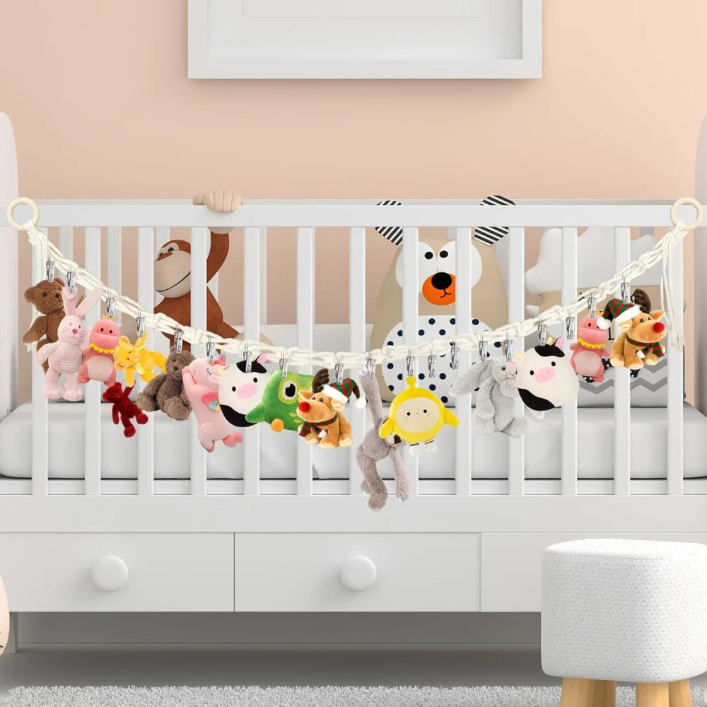 A white crib decorated with a bohemian cotton hanging storage chain featuring various stuffed animal toys.