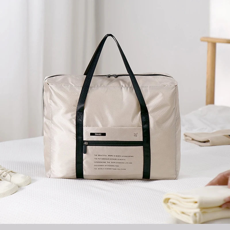 A beige foldable travel duffel bag with black straps resting on a white surface.