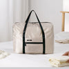A beige foldable travel duffel bag with black straps resting on a white surface.