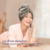 A woman is using a gray towel wrap to dry her hair while talking on a phone.