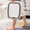 A person holds a white collapsible foot soak bucket with massage dots, resting on a light-colored rug.