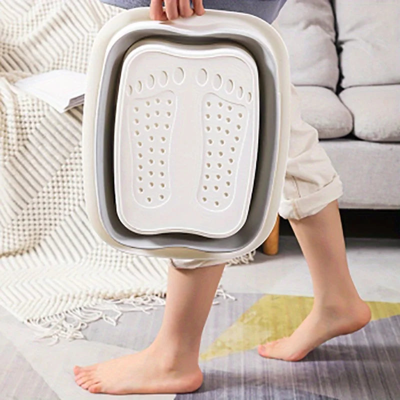 A person holds a white collapsible foot soak bucket with massage dots, resting on a light-colored rug.
