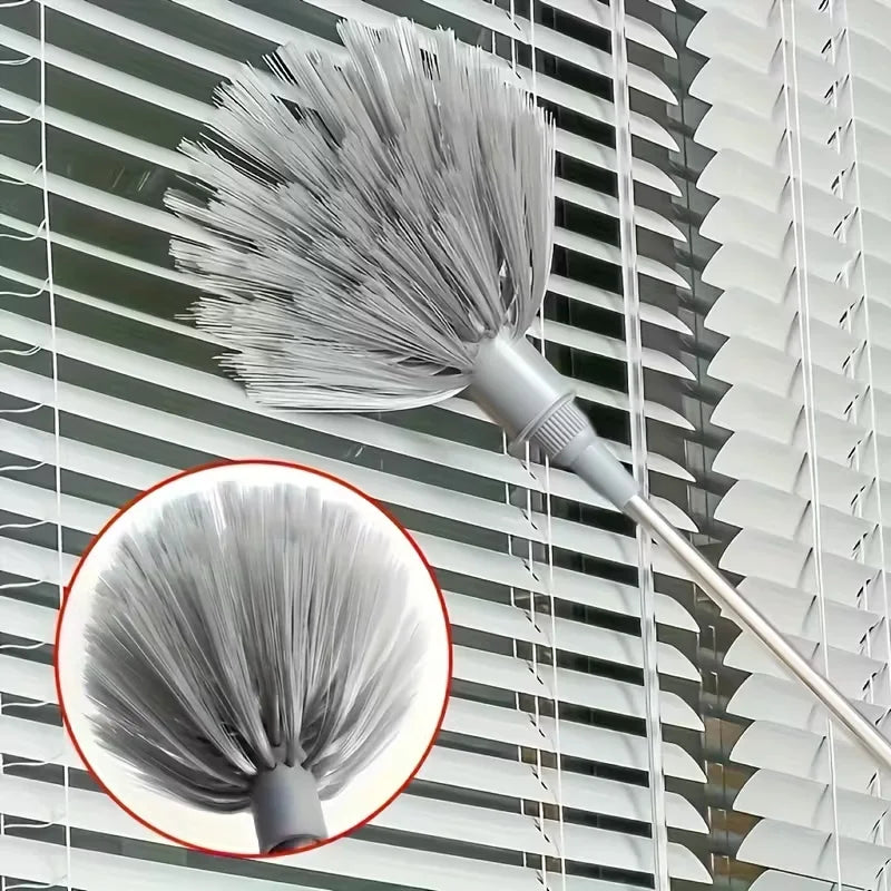 A silver metal cleaning broom with a dense, fluffy head is mounted on a modern window blind.