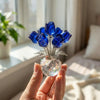 A hand holds a crystal rose flower figurine with blue glass petals and a clear glass vase.