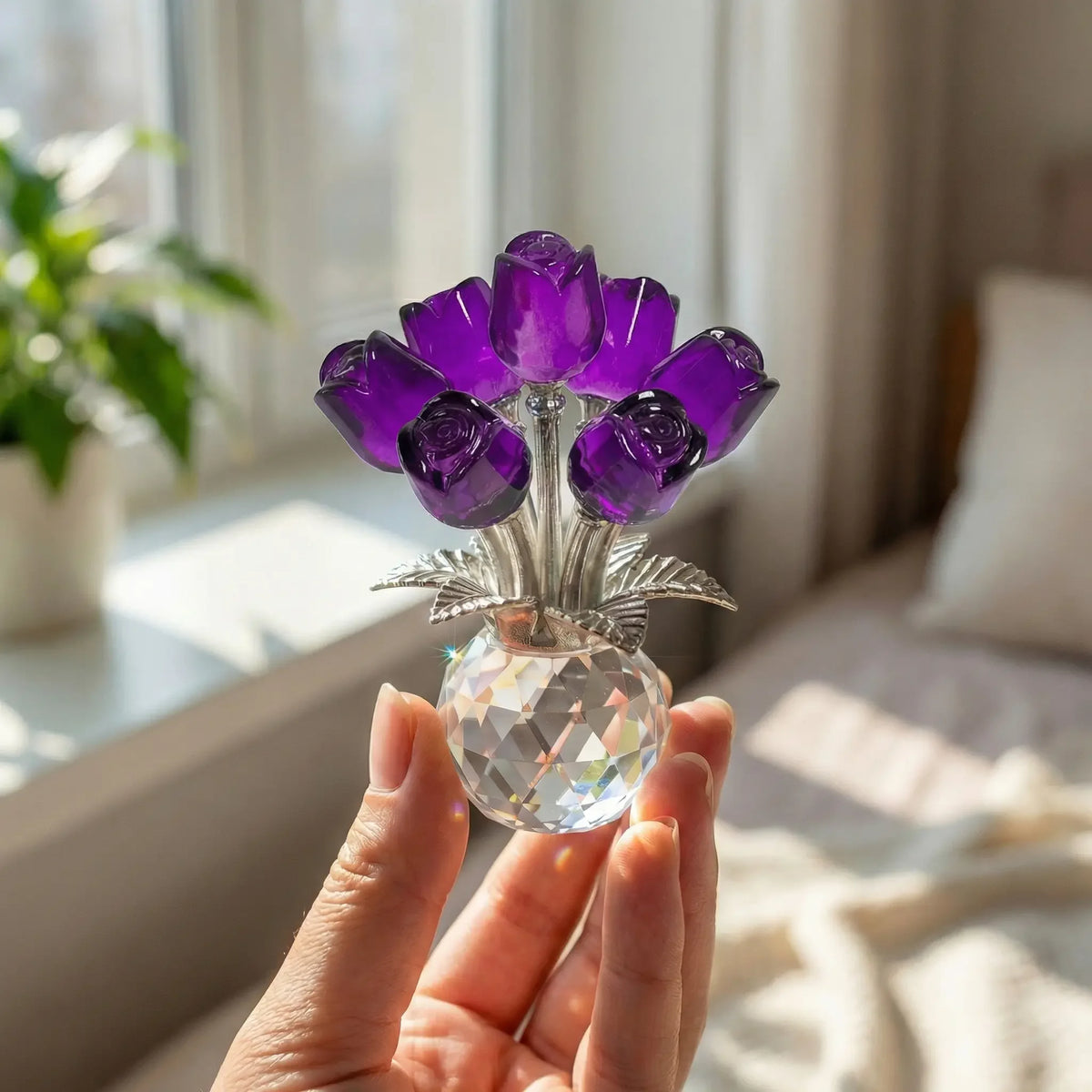 A hand holds a crystal rose flower figurine with purple petals and a clear glass vase.