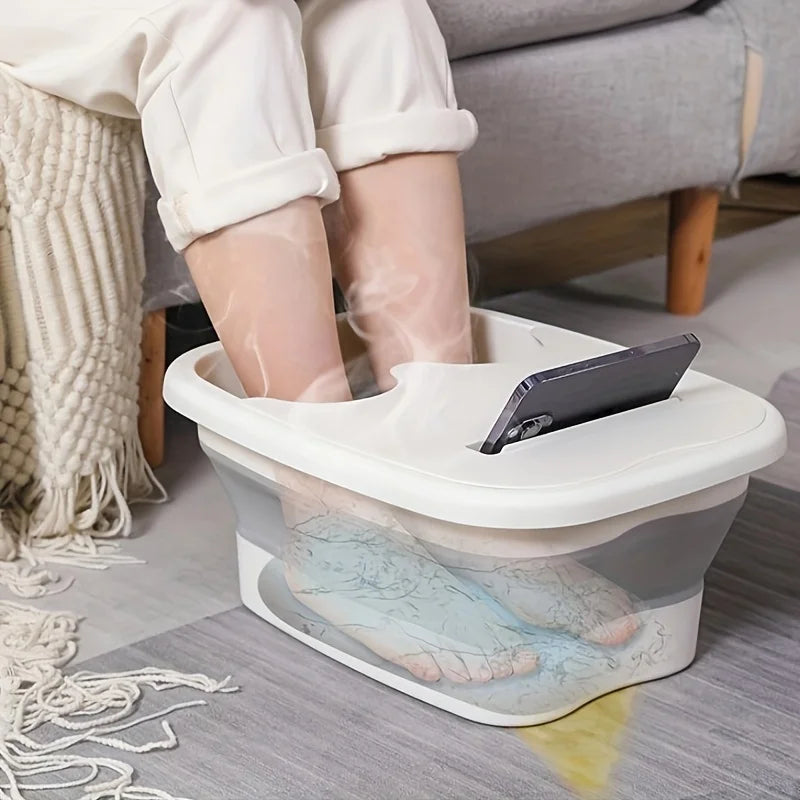 A white collapsible foot soak bucket containing water and massage dots, positioned on a gray floor.