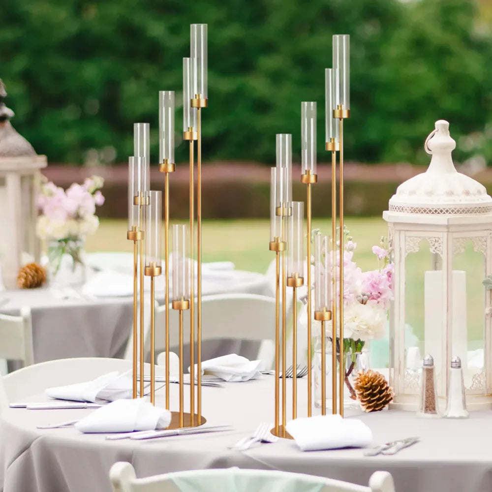 Centro de mesa candelero de 7 brazos dorado con velas de vidrio altas sobre una mesa blanca.