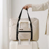 A beige foldable travel duffel bag is being held over a white suitcase.