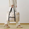 A person holds a beige foldable travel duffel bag with a luggage sleeve.