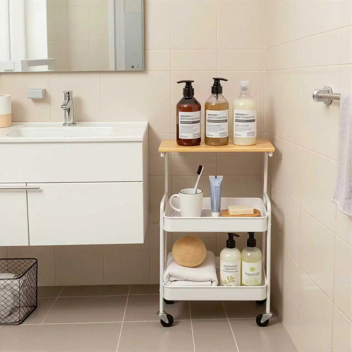 A white 3-tier rolling storage cart with a wooden top holding various liquid soaps and toiletries in a bathroom setting.
