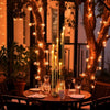 Centro de mesa con candelabro de 7 brazos de oro, exhibido en una mesa de madera al aire libre.