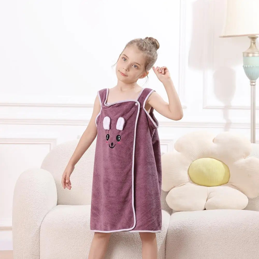 A young girl wearing a purple microfiber bath towel wrap with bunny ears stands in a bright room.