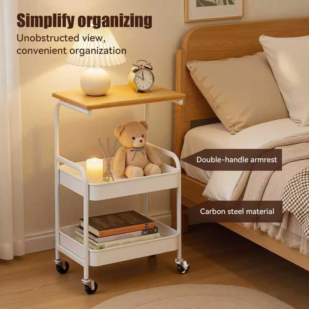 A white 3-tier rolling storage cart with a wooden top, holding a lamp and a teddy bear, next to a wooden bed frame.