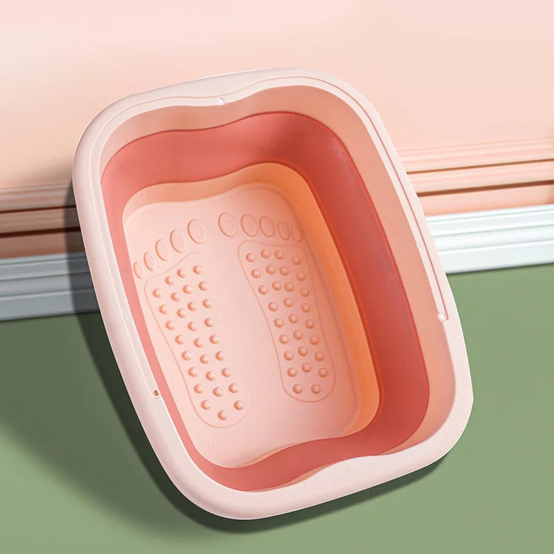 A pink collapsible foot soak bucket with massage dots resting on a green surface.