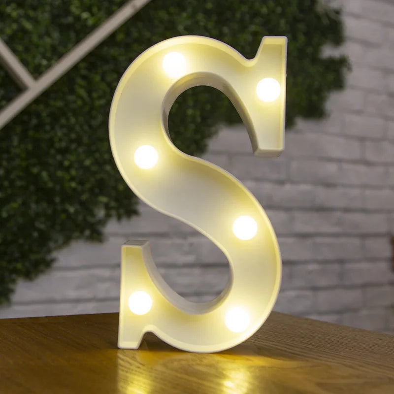A white, illuminated letter S made of LED lights resting on a wooden surface.