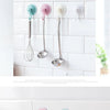A set of silicone spoons with suction cup hooks hanging on a white tiled wall.