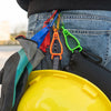 A close-up of a durable glove clip with an ergonomic buckle attached to a denim pocket and a yellow hard hat.