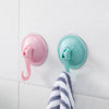 A pink suction cup hook and a teal suction cup hook are mounted on a white wall, with a striped towel below them.