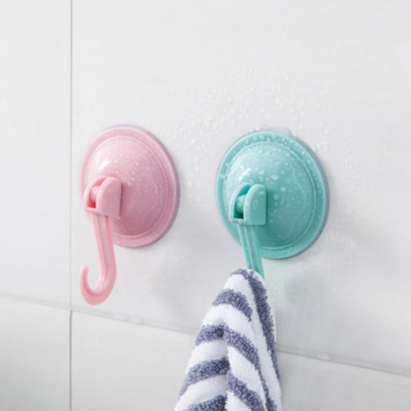 A pink suction cup hook and a teal suction cup hook are mounted on a white wall, with a striped towel below them.