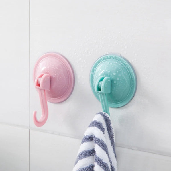 A pink suction cup hook and a teal suction cup hook are mounted on a white wall, with a striped towel below them.