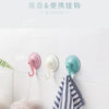 Three silicone suction cup hooks in pink, white, and teal mounted on a white wall.