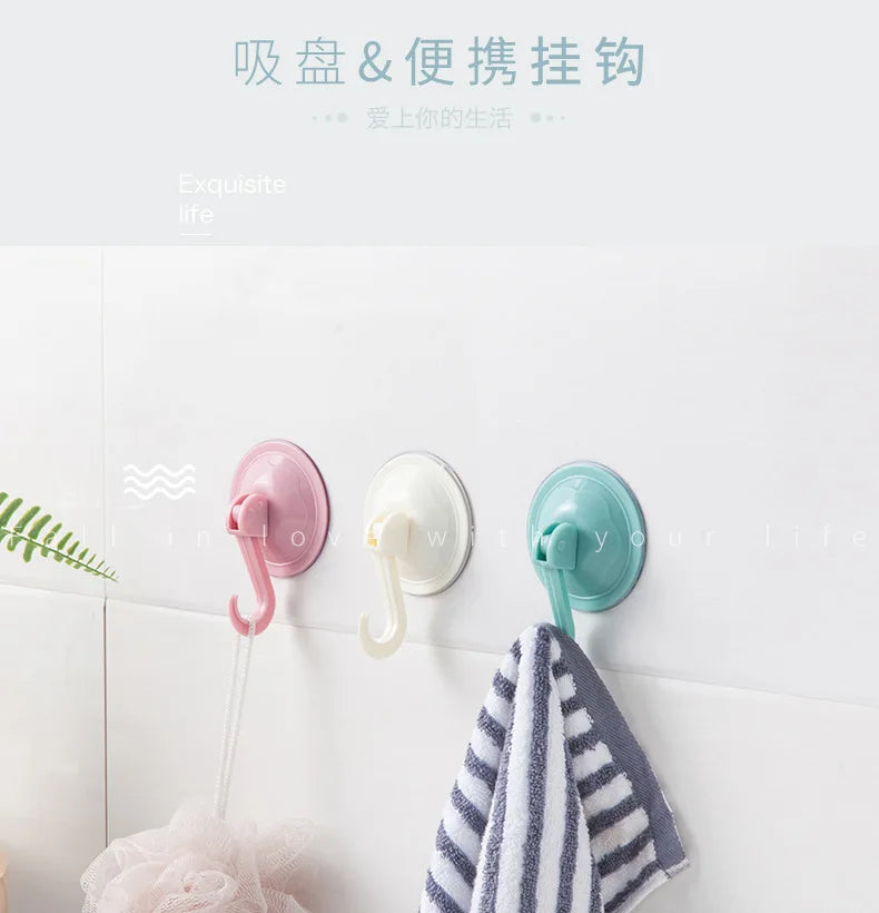 Three silicone suction cup hooks in pink, white, and teal mounted on a white wall.