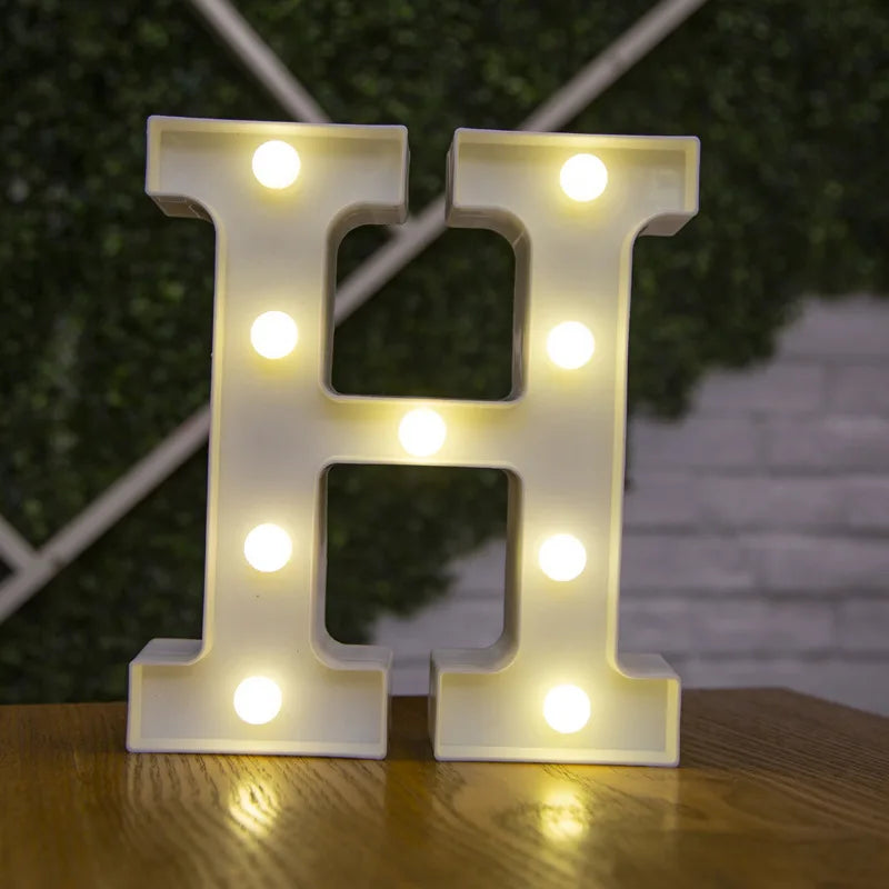 A white alphabet letter H made of LED lights is displayed on a wooden surface.