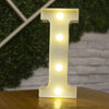 A glowing white letter I made of LED lights standing on a wooden surface.
