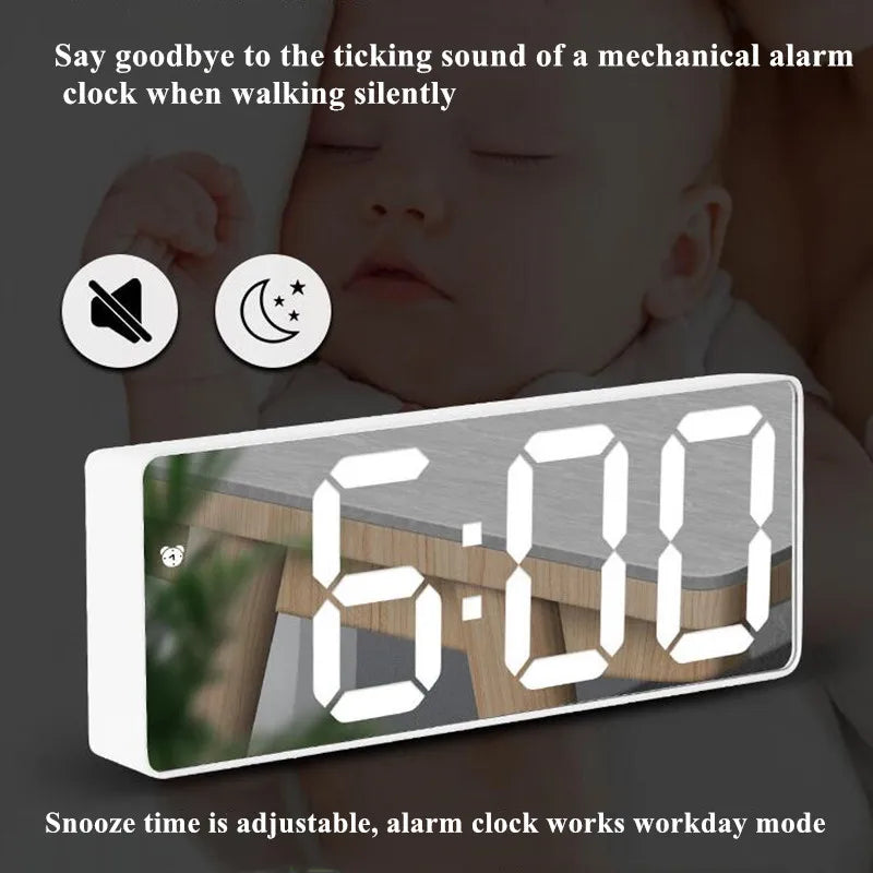 A digital alarm clock displaying 6:00 on a wooden surface, shown in use with a baby.