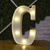 A white illuminated letter C made of LED lights resting on a wooden surface.