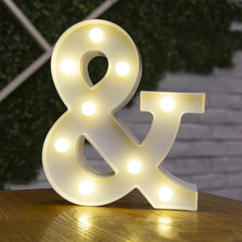 A white alphabet and ampersand sign made of LED lights resting on a wooden surface.