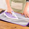 A hand is ironing a fabric using a purple and white high-temperature protection iron on a gray cloth.