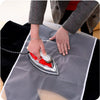 Hands are ironing a piece of fabric with a silver iron on a gray cloth surface.
