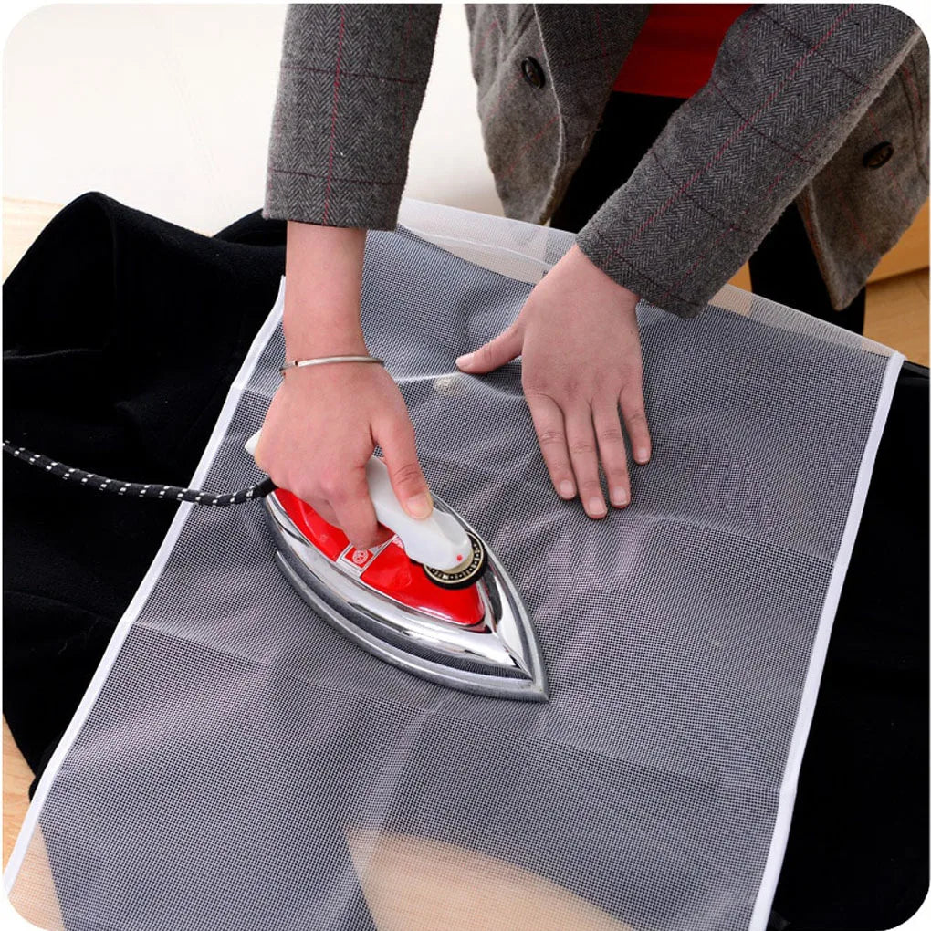 Hands are ironing a piece of fabric with a silver iron on a gray cloth surface.