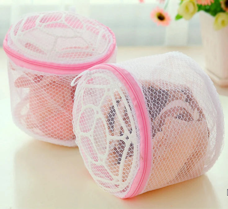 A pink reusable mesh bag for washing lingerie, shown on a white surface.