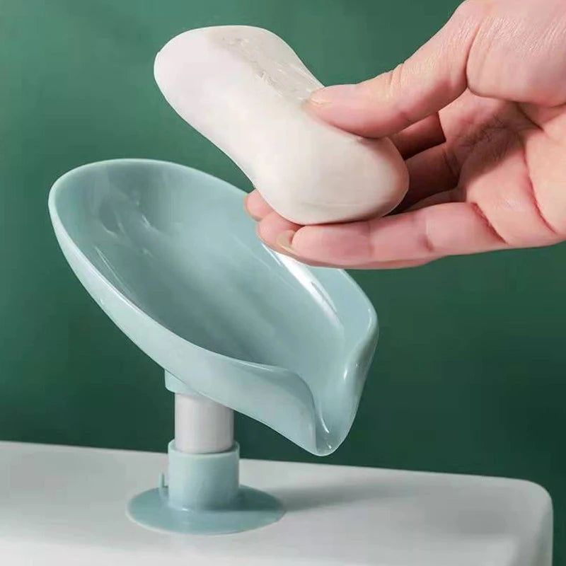 A hand holds a white leaf-shaped suction cup soap holder with a light blue draining tray.
