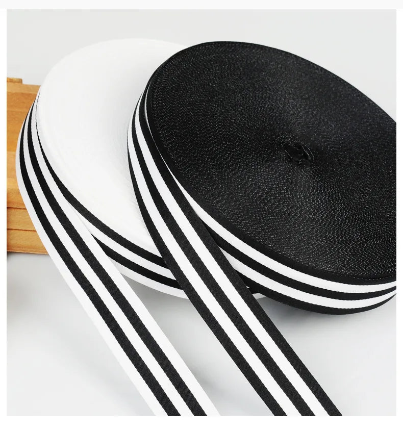 Two black and white grosgrain ribbon rolls are shown, one rolled flat and the other partially unrolled.