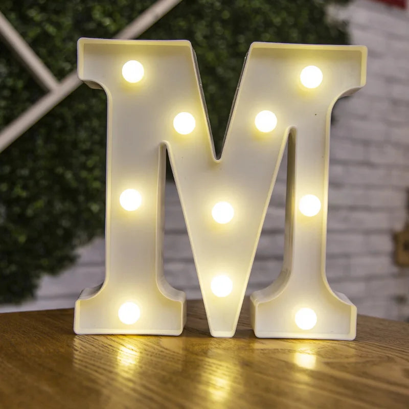 A large, illuminated letter M made of white acrylic with embedded LED lights on a wooden surface.