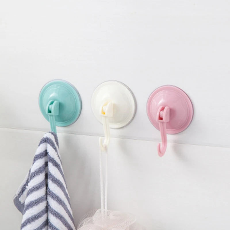 Three colored suction cup hooks—teal, white, and pink—are mounted on a white surface next to a striped towel.