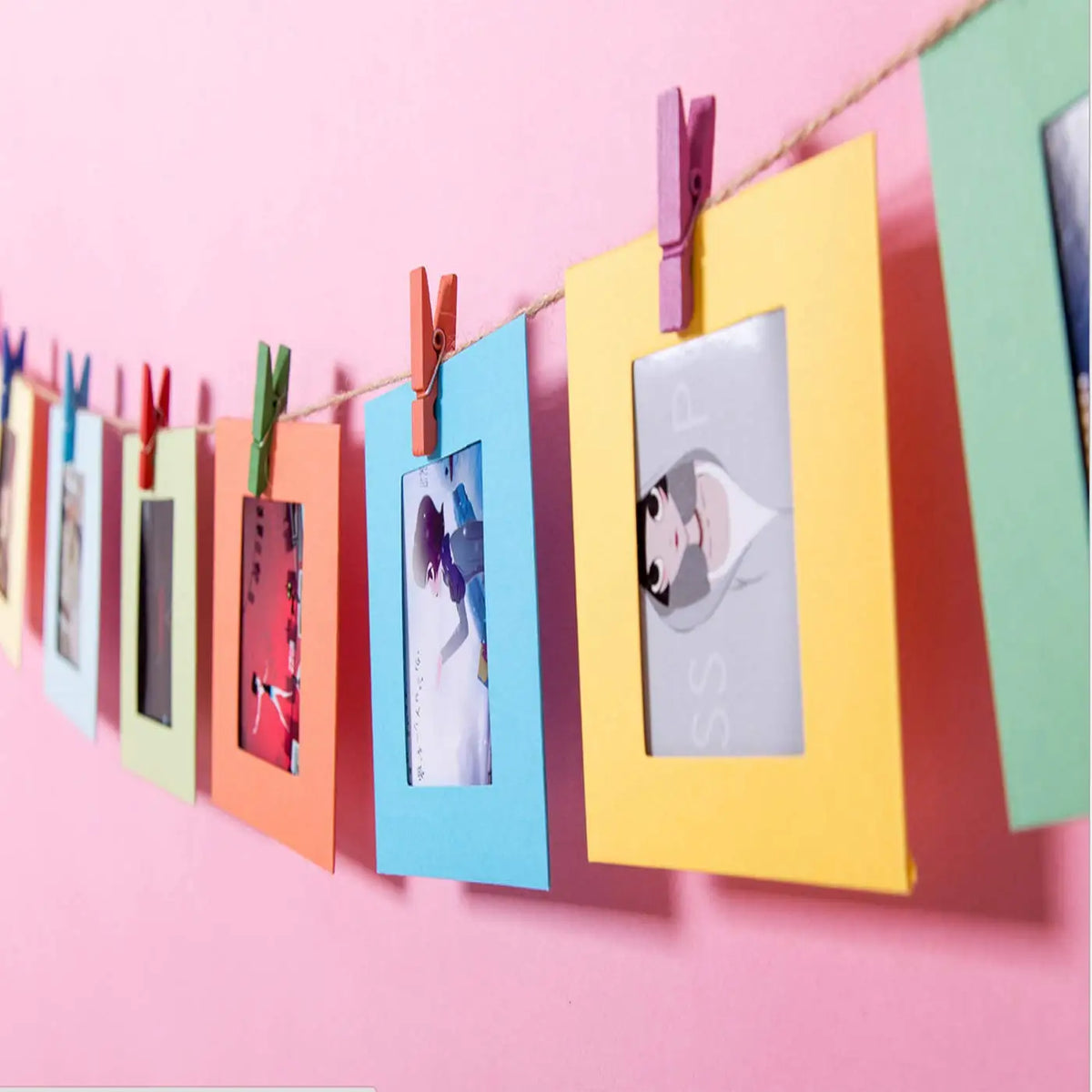Un juego de marcos de fotos de papel coloridos colgados en una cuerda contra un fondo rosa.