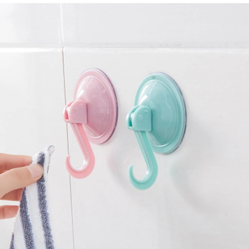 Two plastic suction cup hooks in pink and mint green mounted on a white tile wall.