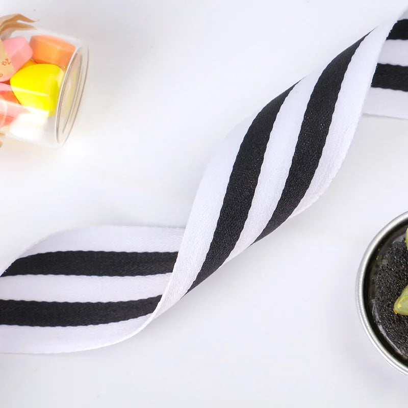 A black and white striped grosgrain ribbon is shown diagonally on a white background next to colorful plastic beads.