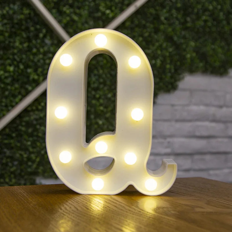 A white, illuminated letter Q made of LED lights resting on a wooden surface.