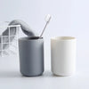 A gray cup and a white cup with a brush are displayed on a white surface.