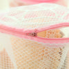 A pink reusable mesh lingerie washing bag with a zipper is shown against a white lace background.