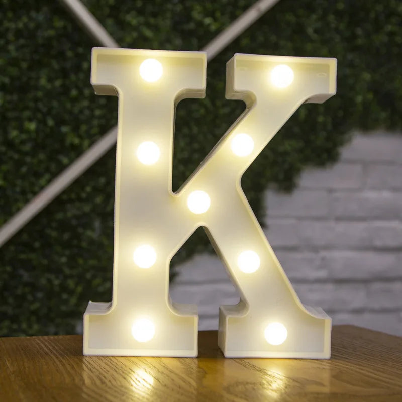 A white illuminated letter K made of LED lights resting on a wooden surface.