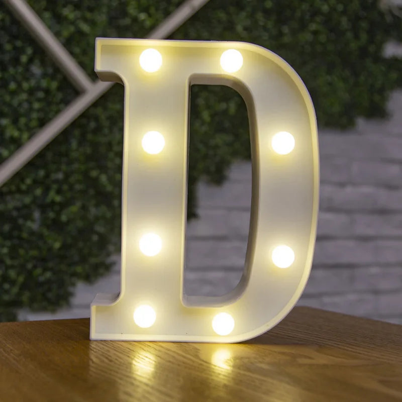 A white illuminated letter D made of LED lights resting on a wooden surface.